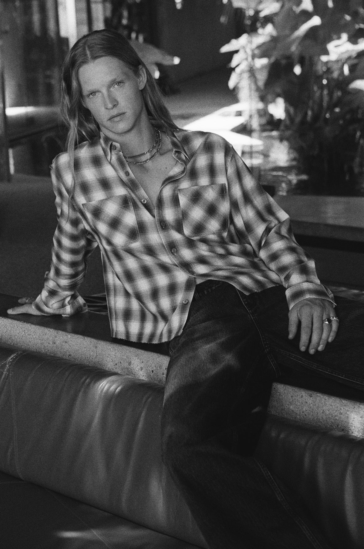 Black-and-white portrait of a model in a checked shirt sitting on a leather sofa.