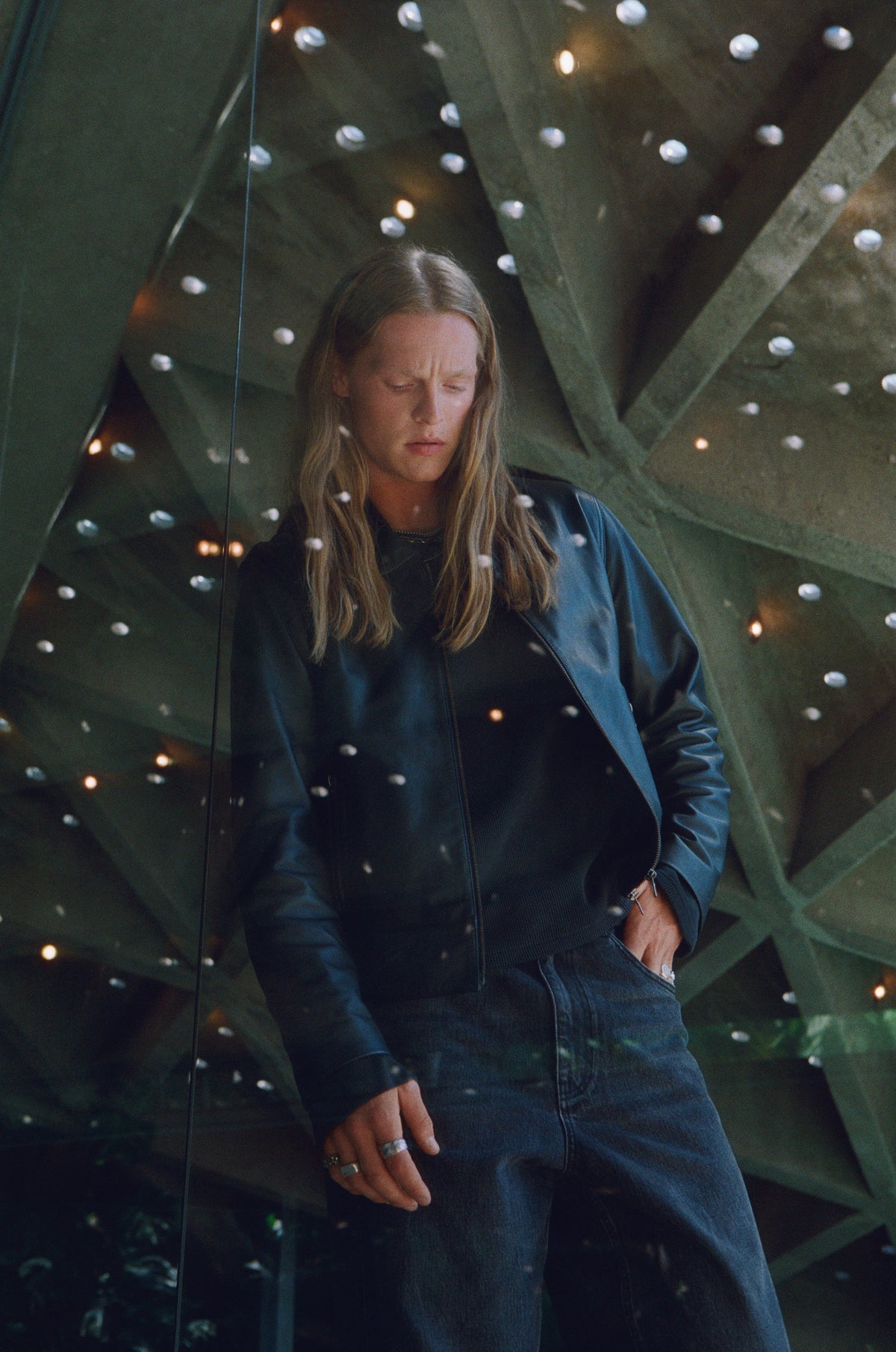 Model in dark denim beneath a geometric concrete ceiling dotted with light.