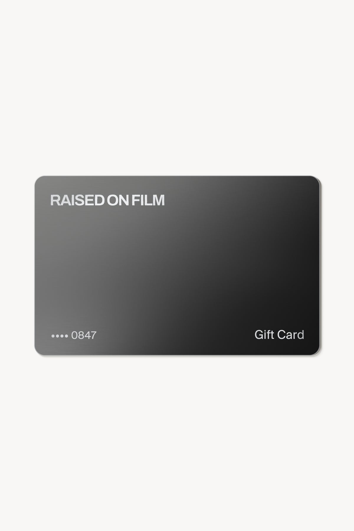 Charcoal Raised on Film gift card with engraved silver lettering on a warm white background