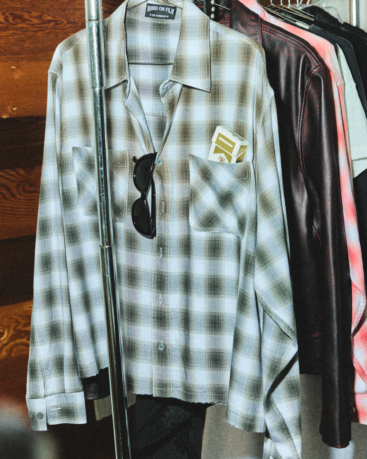 Checked flannel shirts and a leather jacket hanging on a clothing rail.