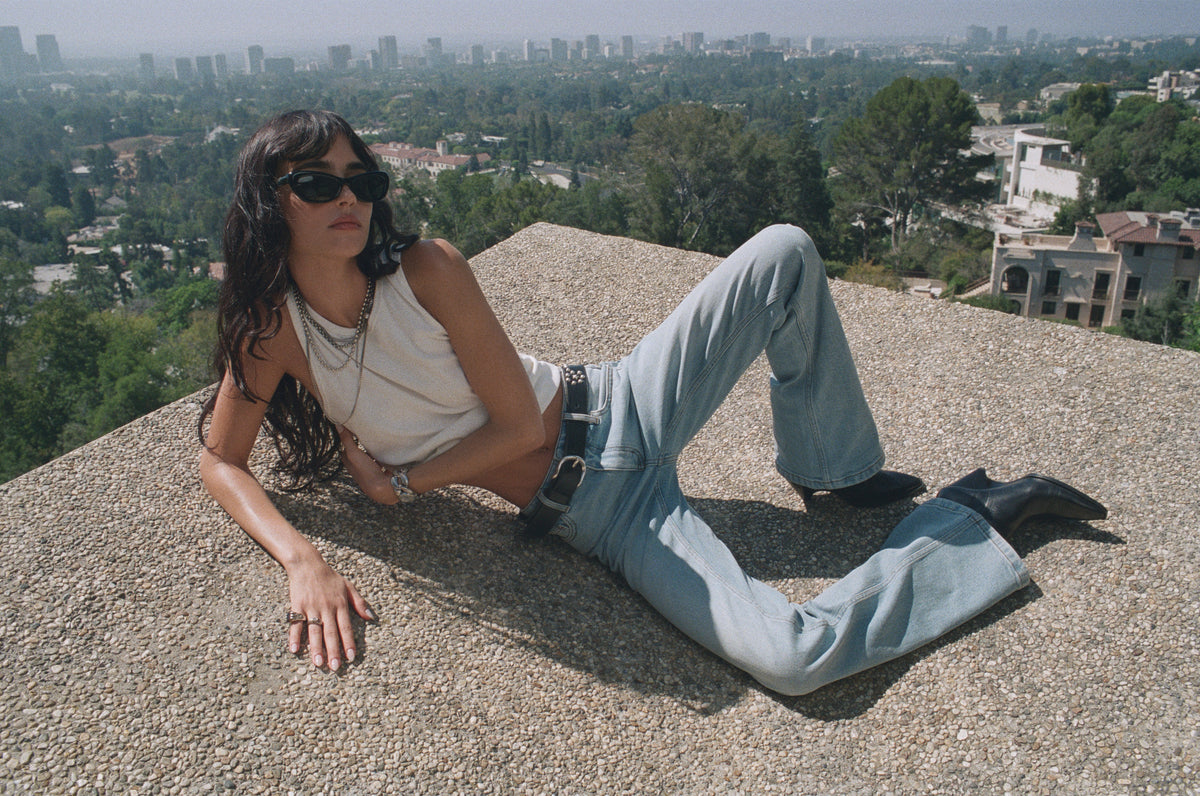 Model in sunglasses and light jeans reclining above the Los Angeles skyline.
