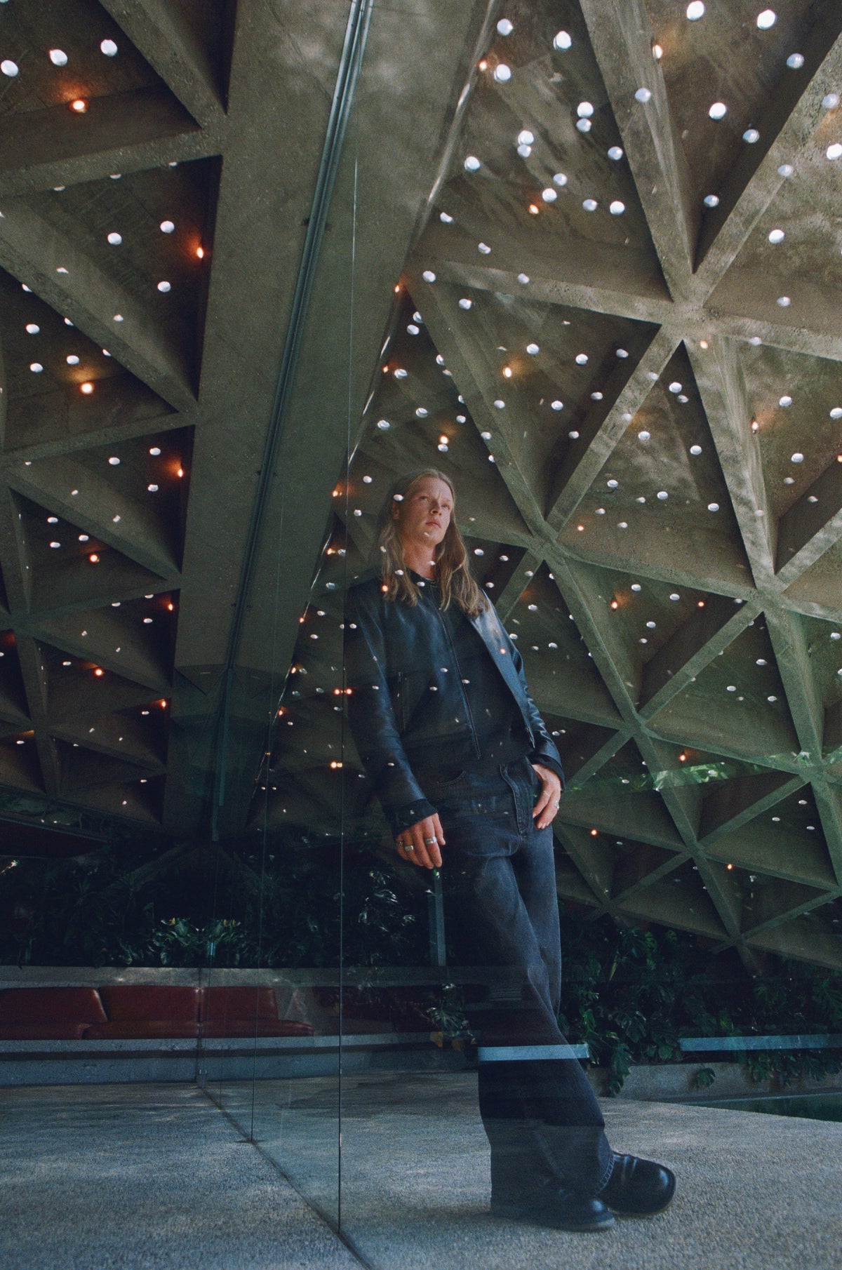 Full-length view of a model in dark denim beneath the angular concrete roof.