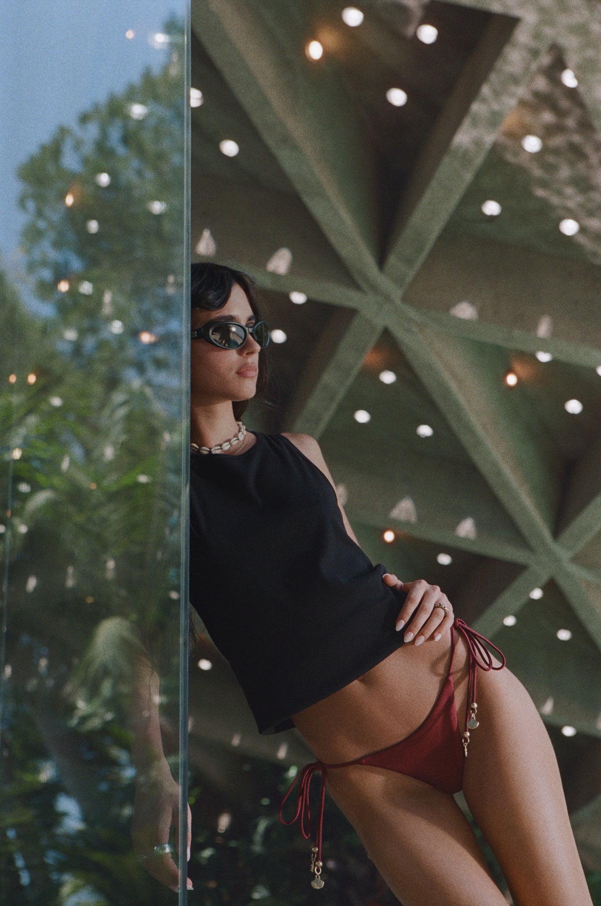 Model in a black cropped top and burgundy bikini beneath the geometric concrete roof.
